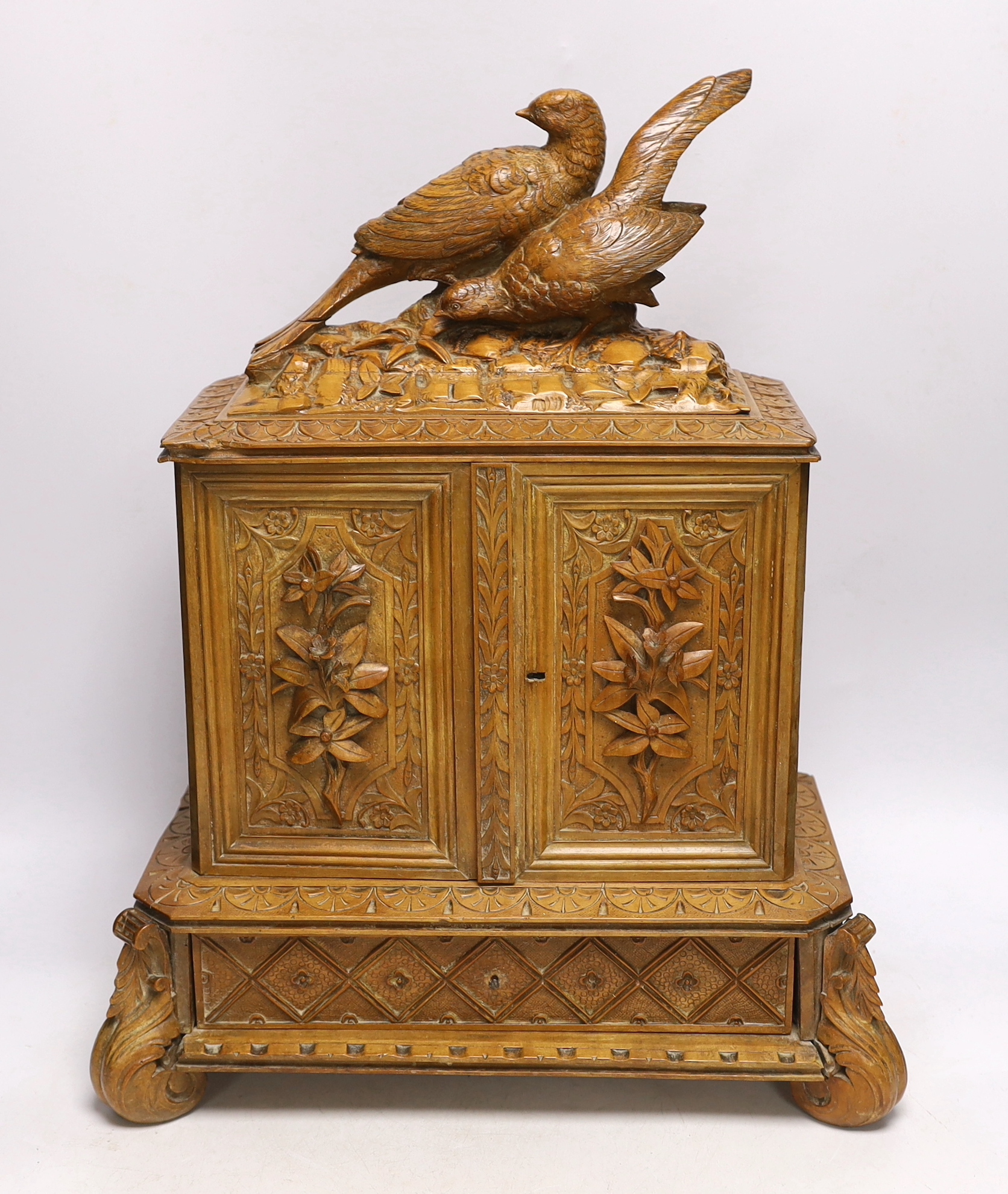 A late 19th century Black Forest carved wooden two door table top cabinet, interior with fitted drawers, surmounted with two pheasants, 51cm high